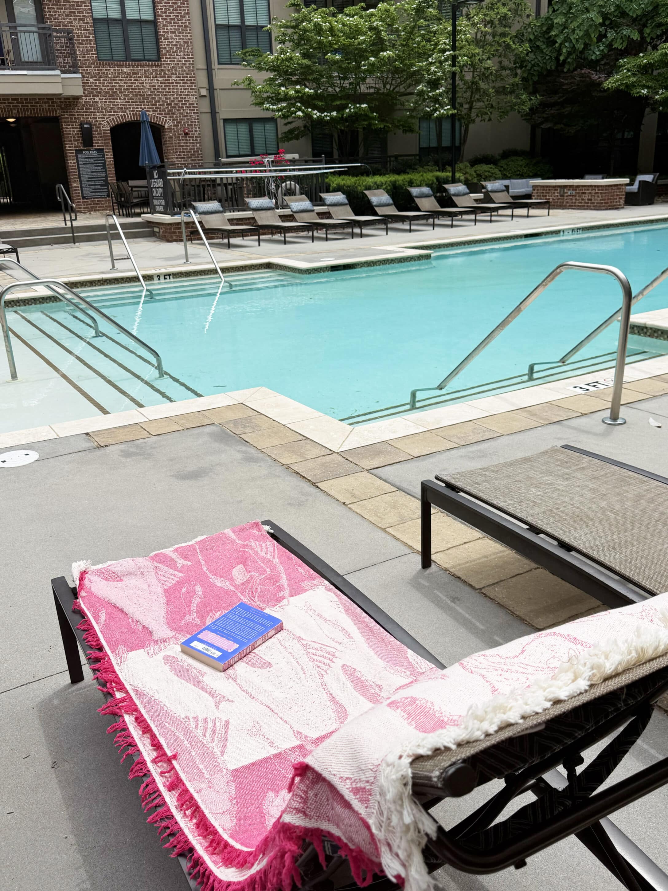 Poolside lounge chairs with pink patterned towels and a book resting on one chair by a turquoise pool.