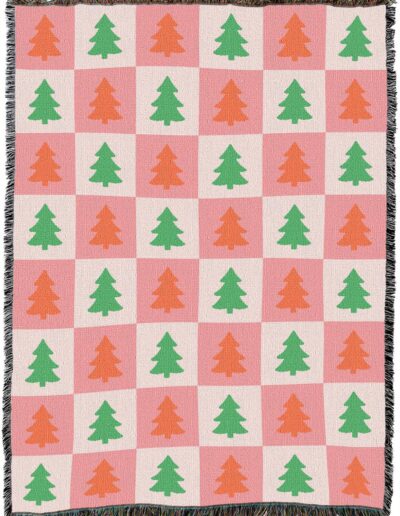 Woven throw blanket with a pink and cream checkered pattern featuring alternating green and orange pine trees.