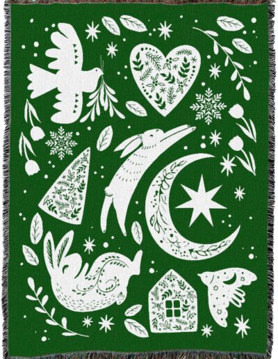 Green woven throw blanket featuring a repeating white pattern of rabbits, birds, a heart, a crescent moon, a house, and snowflakes.
