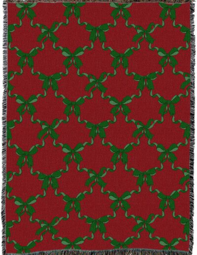 Red woven throw blanket with a repeating pattern of green bows connected by ribbons and fringed edges.