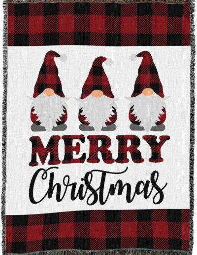 A woven throw blanket featuring three gnomes wearing red and black buffalo plaid hats, with the text Merry Christmas below them and a matching buffalo plaid border at the top and bottom.