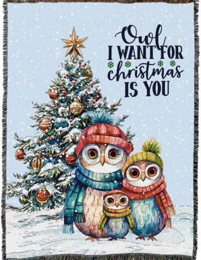 A woven throw blanket featuring a family of three owls in hats and scarves standing in the snow in front of a decorated Christmas tree, with the text Owl I want for Christmas is you.