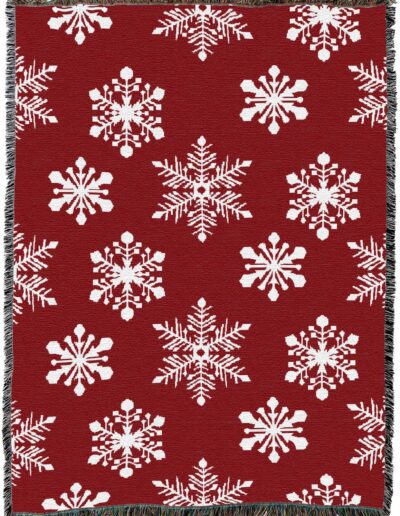 Red throw blanket with a white repeating snowflake pattern and fringed edges.